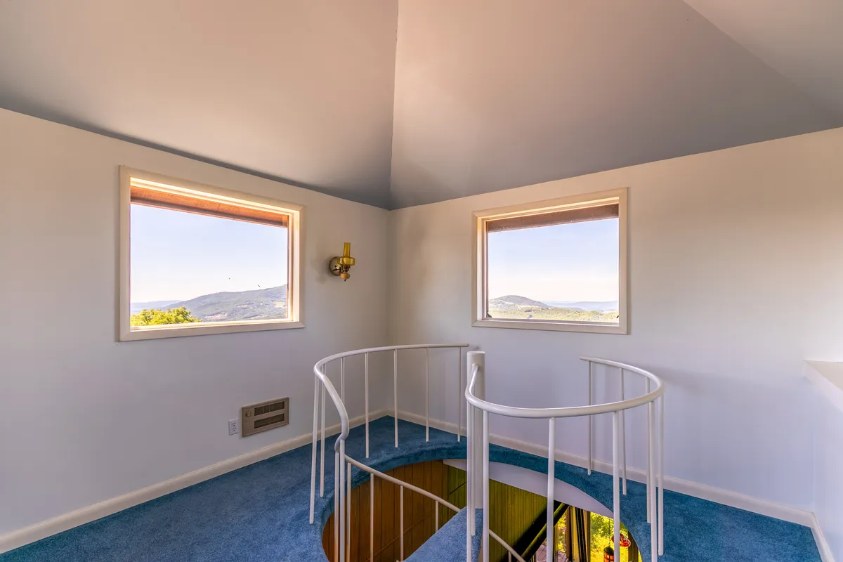 This image presents the crow's nest retreat: a circular space with a railing, plush blue carpet, large windows all around, and a circular opening in the floor. Natural light floods the area, hinting at the sweeping panoramas and tranquil moments described in the section.