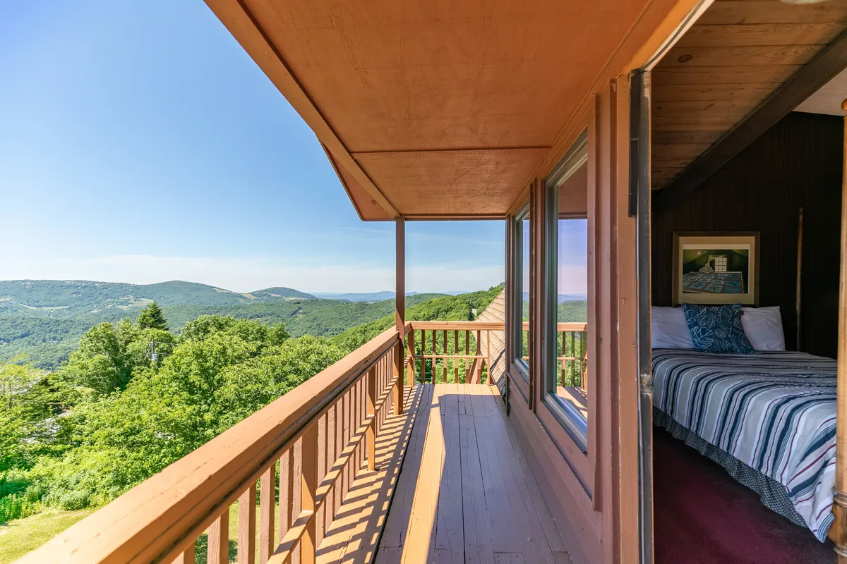 A tranquil balcony overlooks a sweeping mountain landscape, with a cozy bedroom visible just inside. The scene showcases the connection between indoor comfort and stunning natural vistas. The balcony is perfect for enjoying fresh air, while the view stretches across rolling peaks, ideal for observing seasonal changes.