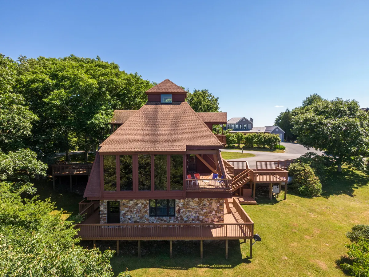 A different angle of the home's unique architectural design, highlighting the expansive deck surrounded by lush greenery. The scene exudes a sense of tranquility and offers a glimpse of the generous outdoor areas ideal for group relaxation and socializing.