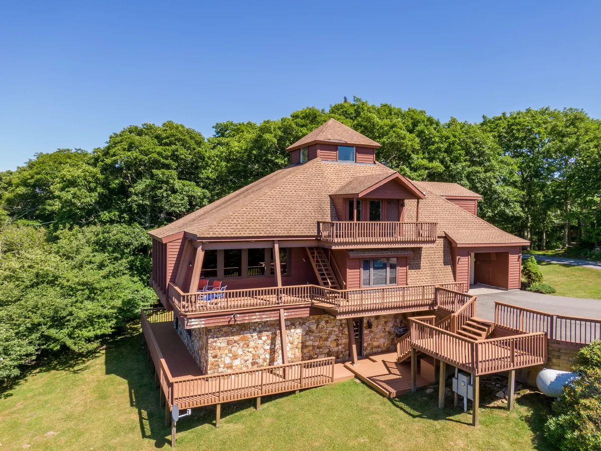A wide view of the home's unique architectural details, expansive deck space, and surrounding greenery. The image emphasizes the inviting, open-air environment and the seamless transition between indoors and outdoors.