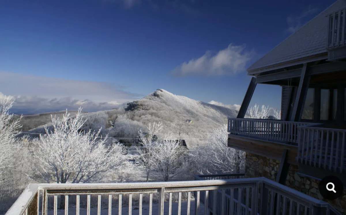 A view of snow-covered mountains and frosted trees seen from a balcony, with a railing framing the sweeping landscape. The tranquil yet invigorating winter scene alludes to skiing, snowboarding, and the unique thrill of high-altitude adventures.