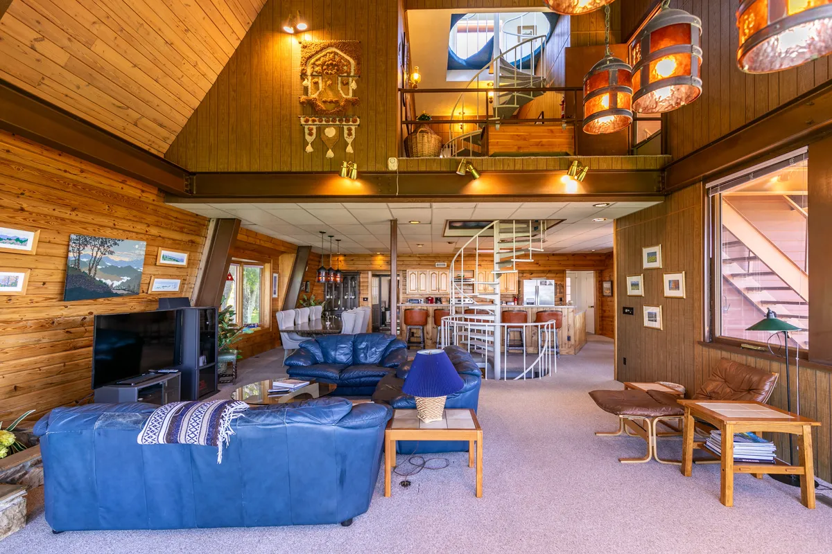 An interior scene featuring a cozy blue leather sofa, the spiral staircase, wooden wall decor, and large windows letting in natural light. The spiral staircase—a key architectural element—takes center stage, highlighting the retro charm and creative possibilities within the home.