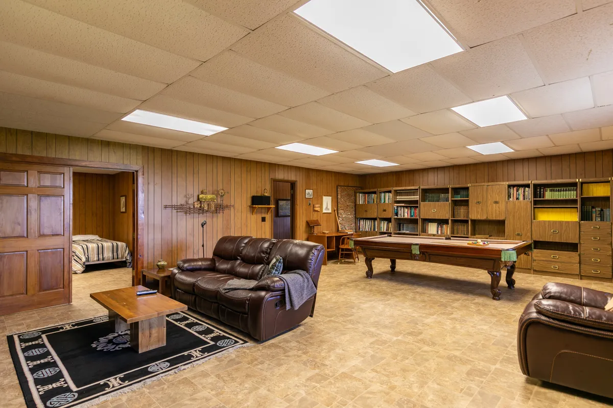 A cozy game and family room with a sofa, pool table, bookshelves, and a coffee table. The layout invites both relaxation and friendly competition, with books and board games readily accessible alongside the pool table.