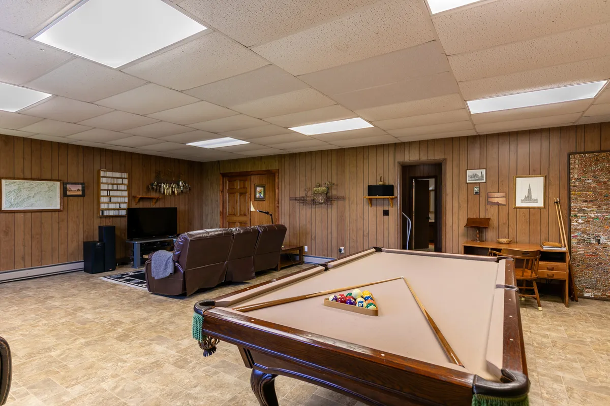 The game room with a pool table, plush sofa seating, a large television, and wood paneling. The relaxed space is clearly set up for group gatherings, whether for playing games or enjoying a movie together.