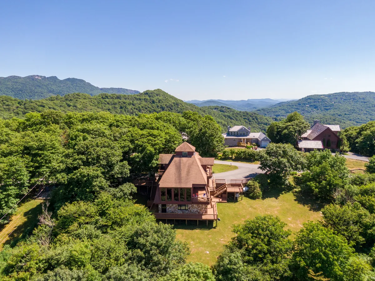 This image showcases the unique architectural design of the house, nestled amid lush greenery with distant mountain views. The exterior highlights the structure's retro character and the sweeping natural landscape surrounding it.
