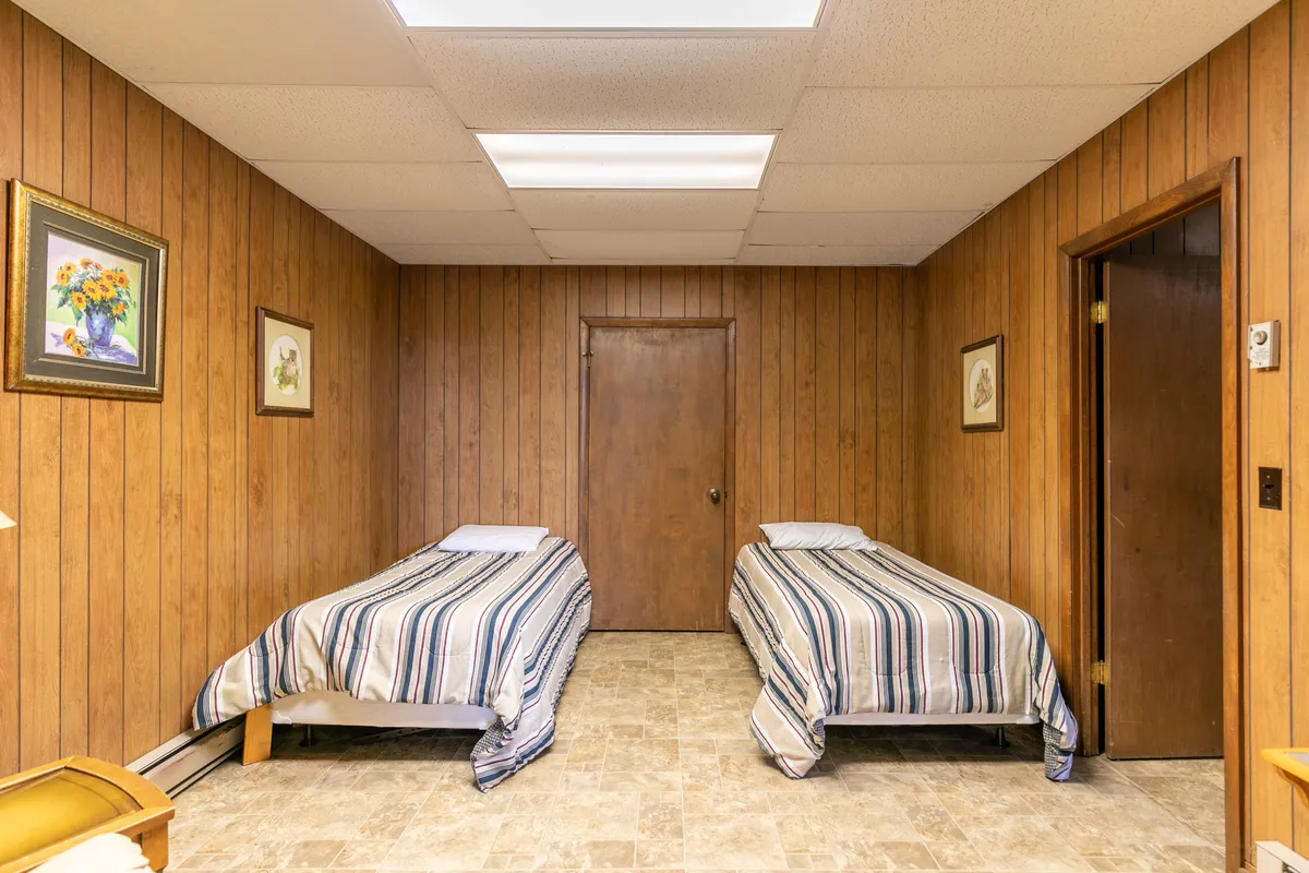A practical sleeping area with two single beds, framed artwork, and a wooden door. The space feels simple yet comfortable, designed for shared moments and quiet rest.