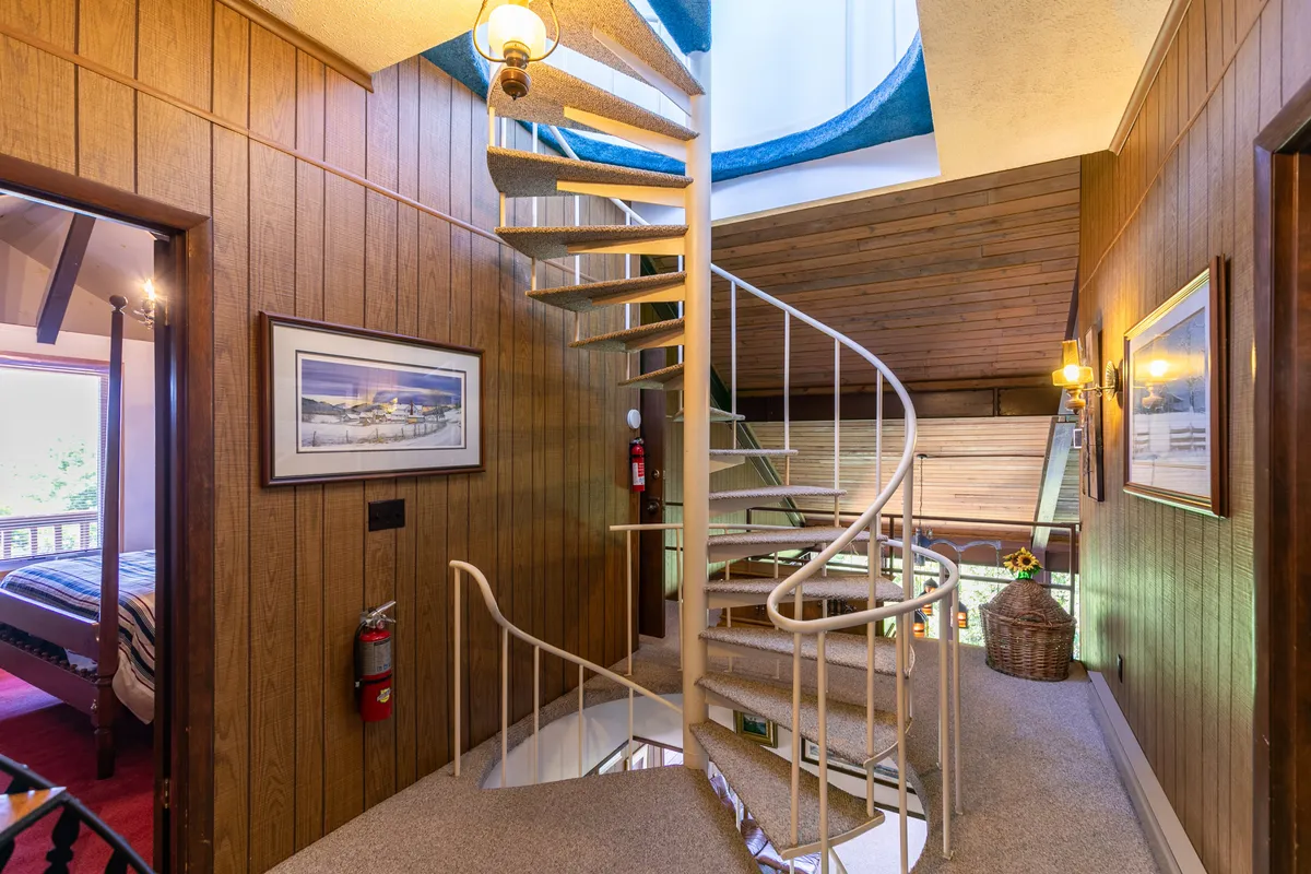 This image showcases the spiral staircase ascending through a warmly illuminated, wood-paneled interior. The staircase is the central architectural feature, flanked by framed artwork and basked in a cozy glow, inviting exploration upwards toward the home's upper levels.