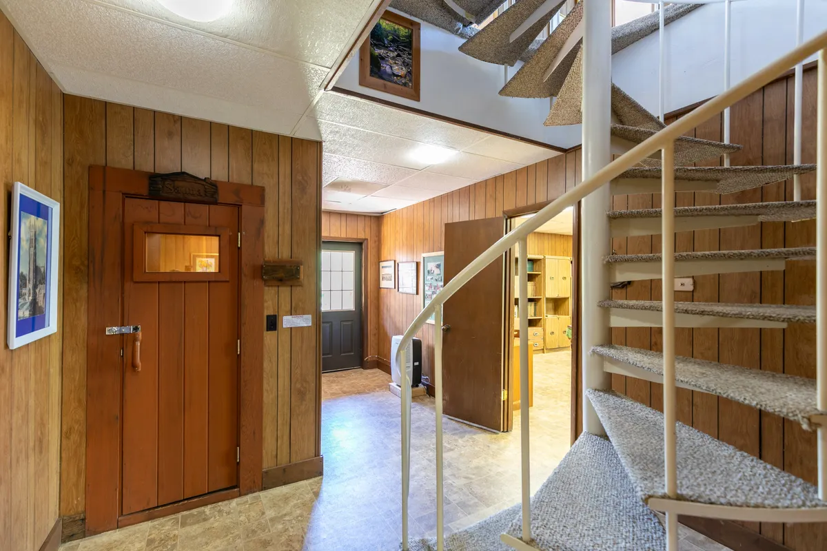 A welcoming view of the spiral staircase at the entryway, with wood paneling, framed pictures, and a wooden door nearby. The perspective captures the beginning of the vertical journey through the home's core architectural element.